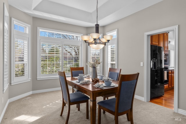 dining room with a tray ceiling, baseboards, a chandelier, and light carpet