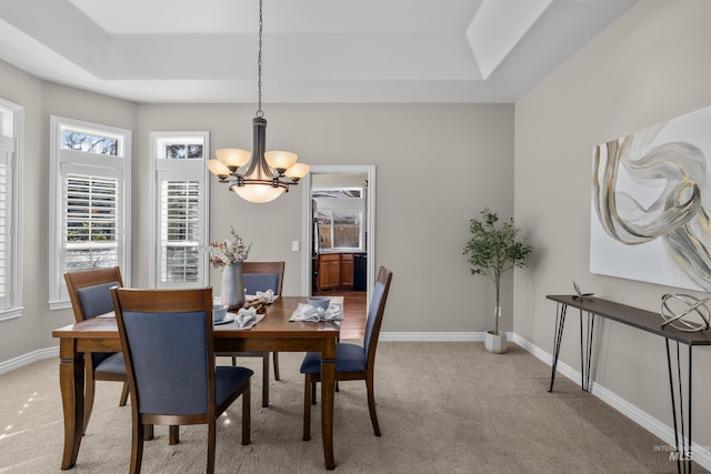 dining space with light colored carpet, an inviting chandelier, a tray ceiling, and baseboards