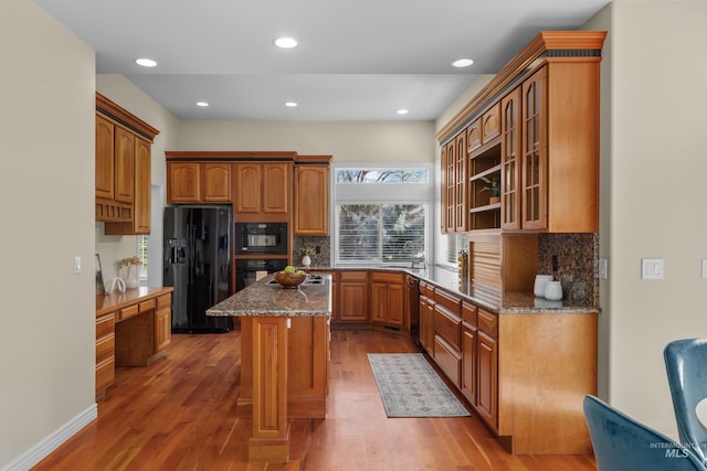 kitchen featuring a center island, black appliances, dark stone counters, and wood finished floors