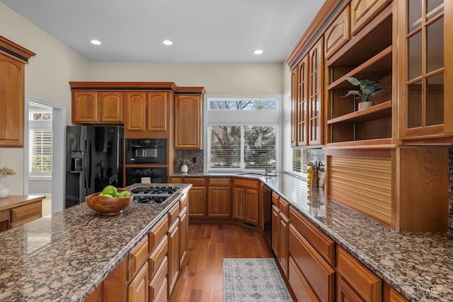 kitchen with dark stone counters, glass insert cabinets, black appliances, and dark wood-style flooring