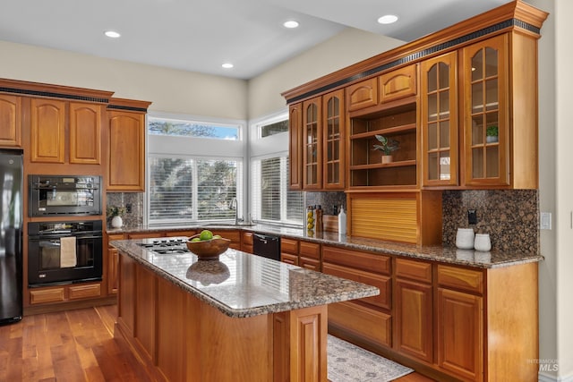 kitchen with black appliances, glass insert cabinets, light wood-style floors, and dark stone counters