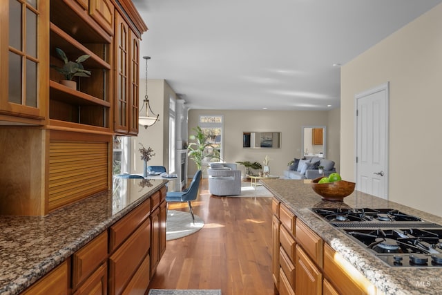 kitchen featuring dark wood finished floors, dark stone counters, glass insert cabinets, stovetop with downdraft, and open floor plan