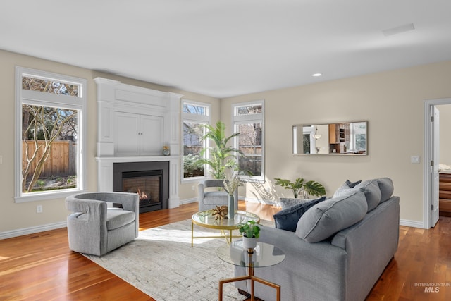 living area with baseboards, a lit fireplace, and wood finished floors