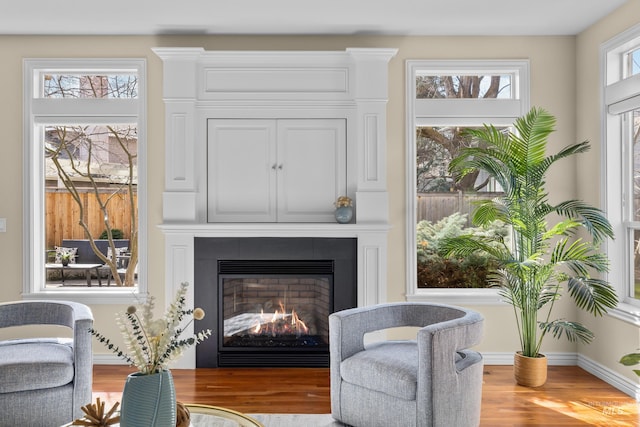 sitting room with baseboards, a warm lit fireplace, and wood finished floors