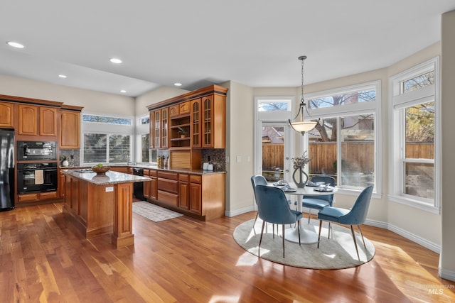 kitchen with light stone counters, light wood-style flooring, black appliances, glass insert cabinets, and brown cabinets