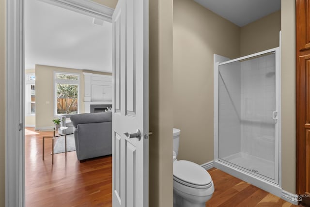 full bath featuring wood finished floors, baseboards, a fireplace, a stall shower, and toilet