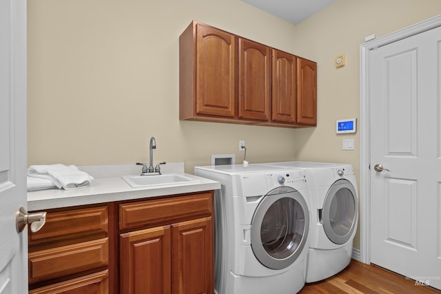 laundry room featuring cabinet space, washer and dryer, wood finished floors, and a sink