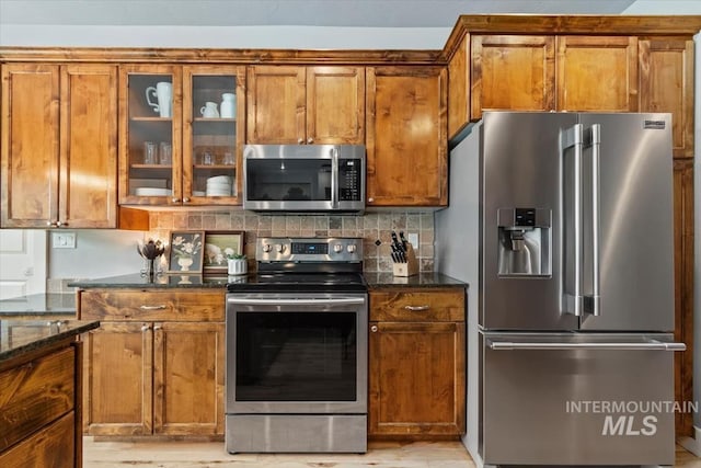 12231 W Caribee Inlet Dr, Star, ID 83669 - kitchen featuring stainless steel appliances, brown cabinetry, dark stone countertops, glass insert cabinets, and backsplash