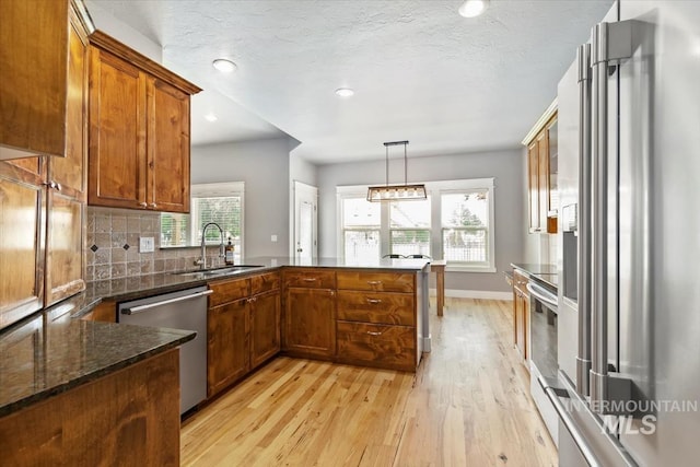 12231 W Caribee Inlet Dr, Star, ID 83669 - kitchen featuring stainless steel appliances, a peninsula, light wood finished floors, brown cabinets, and dark stone counters