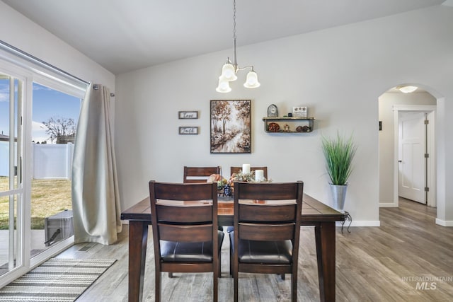 dining area featuring arched walkways, a chandelier, baseboards, and wood finished floors