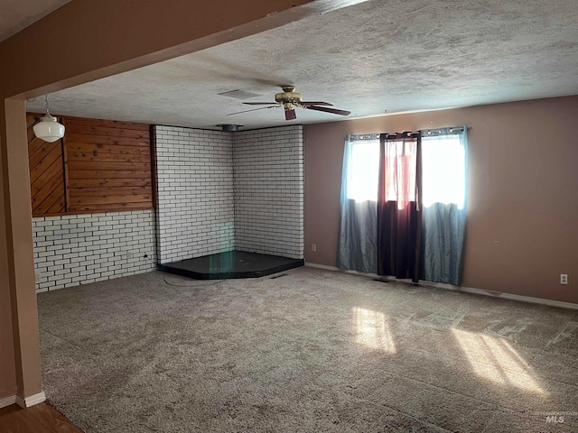 carpeted empty room with a textured ceiling, brick wall, and ceiling fan