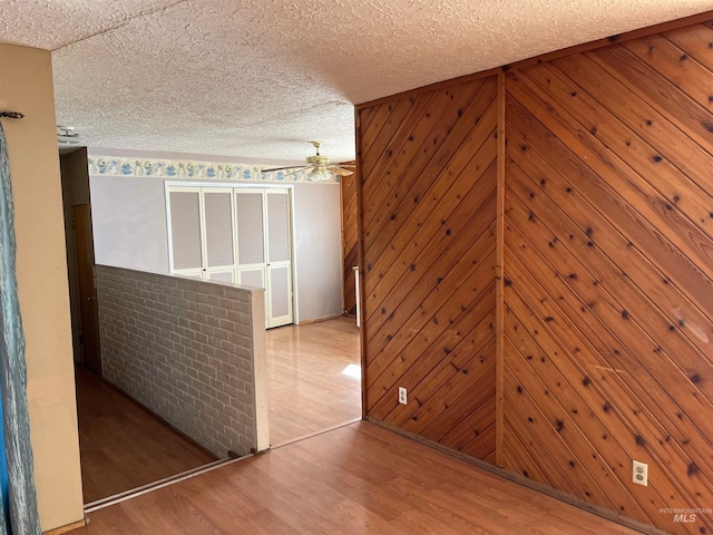 spare room with light hardwood / wood-style floors, a textured ceiling, wooden walls, and ceiling fan