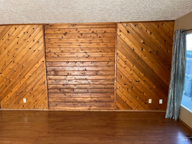 empty room with hardwood / wood-style flooring, a textured ceiling, and wooden walls