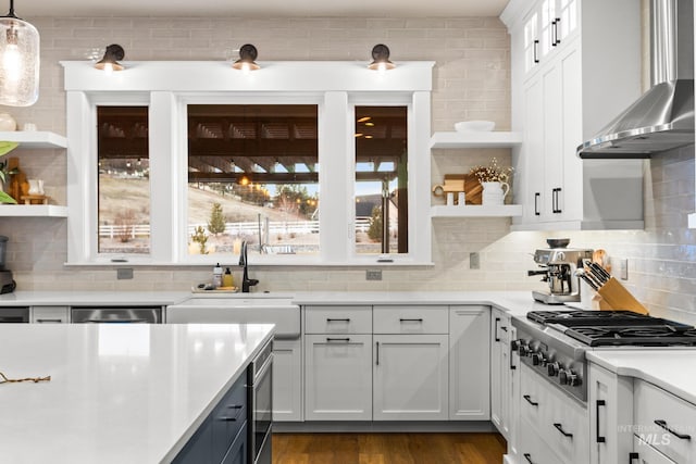 kitchen featuring open shelves, a sink, light countertops, stainless steel gas stovetop, and wall chimney exhaust hood