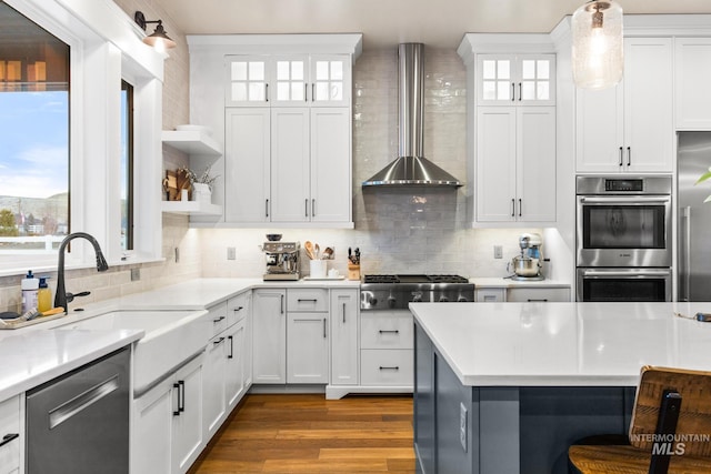 kitchen featuring backsplash, appliances with stainless steel finishes, light countertops, and wall chimney range hood