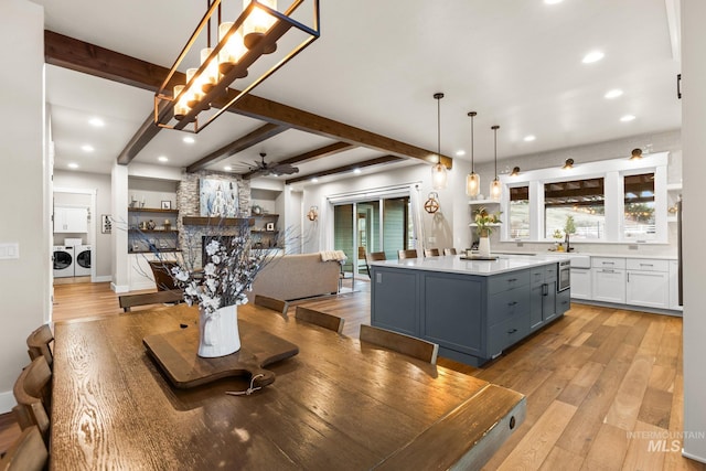 dining room with a ceiling fan, light wood-style flooring, washing machine and dryer, and beamed ceiling