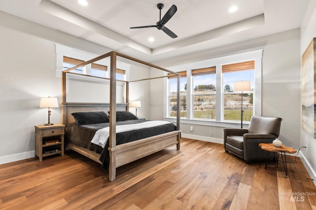 bedroom featuring recessed lighting, baseboards, a raised ceiling, and wood finished floors