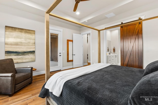 bedroom featuring a raised ceiling, recessed lighting, a barn door, light wood-style floors, and baseboards