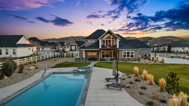 back of house at dusk featuring a fenced backyard, a pool with connected hot tub, a lawn, a patio area, and a mountain view