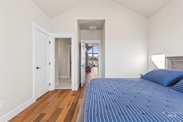 bedroom with visible vents, light wood-style flooring, baseboards, and vaulted ceiling