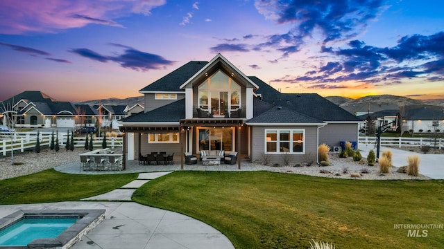 back of house at dusk with an outdoor hot tub, an outdoor living space, a patio, a fenced backyard, and a balcony