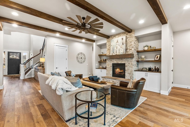 living room featuring light wood-type flooring, baseboards, a stone fireplace, and stairs