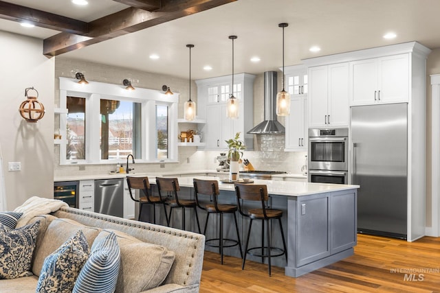 kitchen with beverage cooler, light countertops, appliances with stainless steel finishes, light wood-style floors, and wall chimney exhaust hood