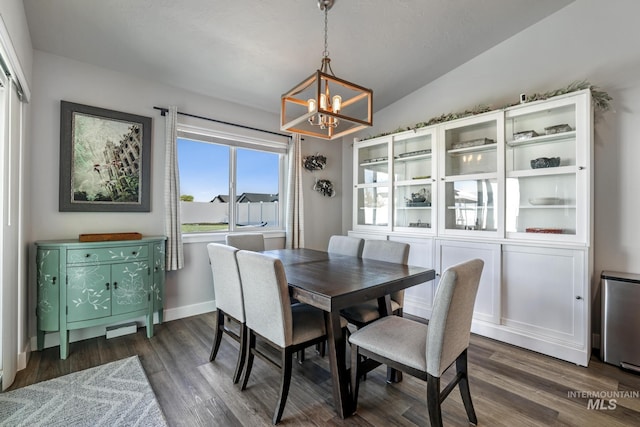 dining room with dark wood-type flooring, a notable chandelier, and vaulted ceiling