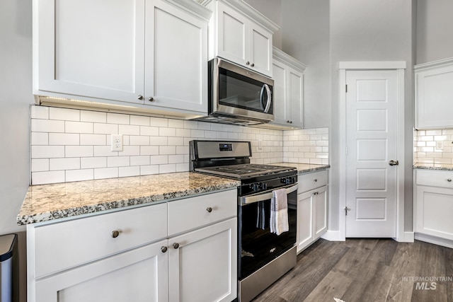 kitchen with dark wood-style floors, appliances with stainless steel finishes, white cabinetry, and decorative backsplash
