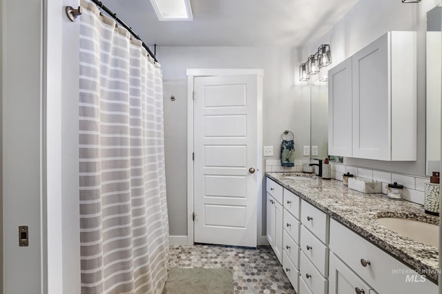 bathroom with baseboards, a shower with shower curtain, double vanity, and a sink