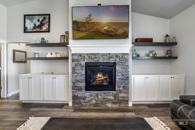 living area featuring dark wood-style flooring, a stone fireplace, and lofted ceiling