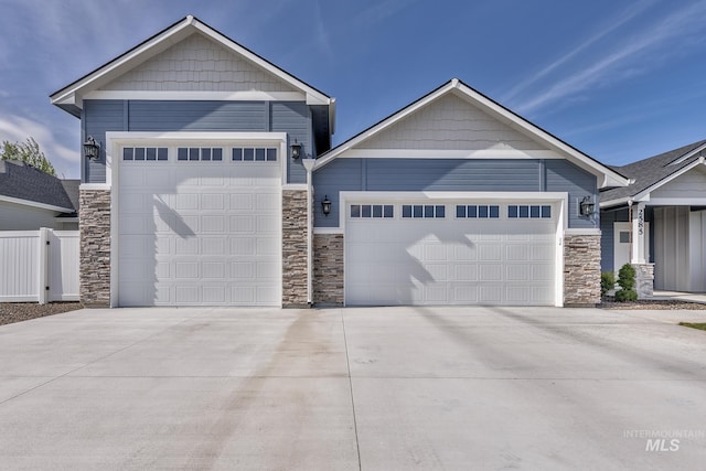 view of front of house with stone siding, a garage, concrete driveway, and fence