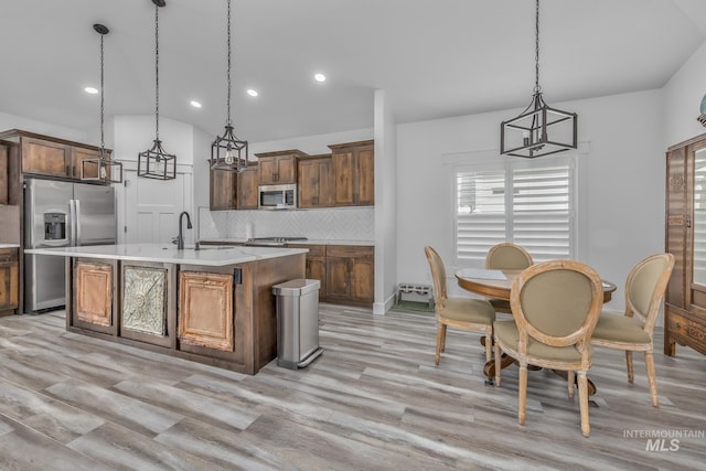 kitchen featuring appliances with stainless steel finishes, light countertops, light wood-style floors, backsplash, and hanging light fixtures