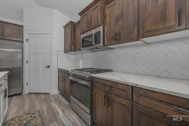 kitchen with appliances with stainless steel finishes, backsplash, light wood-type flooring, light stone counters, and dark brown cabinets