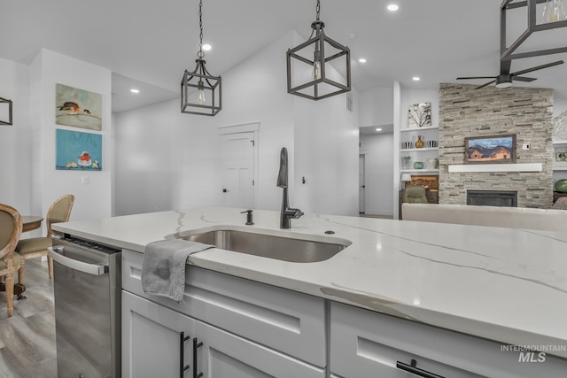 kitchen with a sink, ceiling fan, light stone countertops, vaulted ceiling, and a fireplace