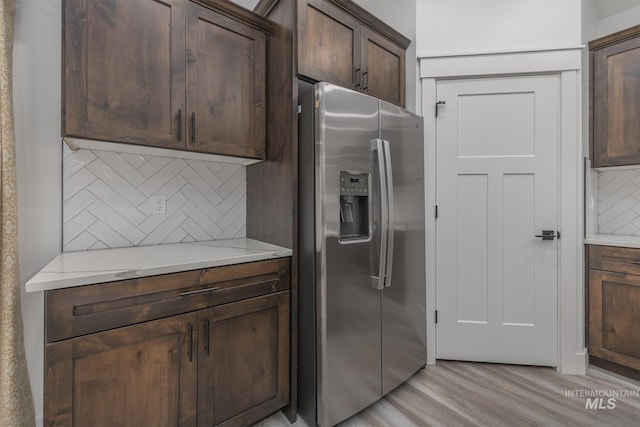 kitchen featuring stainless steel fridge with ice dispenser, tasteful backsplash, light wood finished floors, and dark brown cabinets
