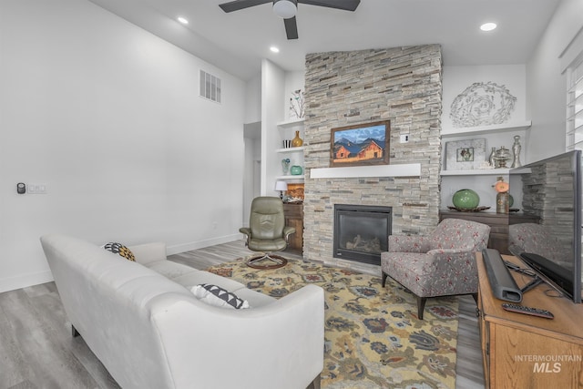 living area featuring wood finished floors, a stone fireplace, baseboards, ceiling fan, and recessed lighting