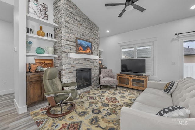 living area featuring a stone fireplace, ceiling fan, lofted ceiling, light wood-type flooring, and recessed lighting