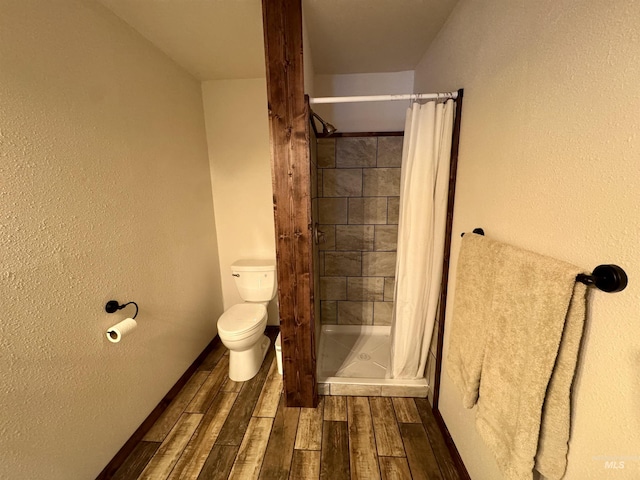 bathroom with a textured wall, toilet, wood finish floors, baseboards, and a stall shower