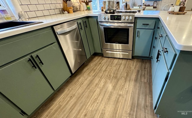 kitchen featuring stainless steel appliances, light countertops, backsplash, light wood finished floors, and green cabinetry