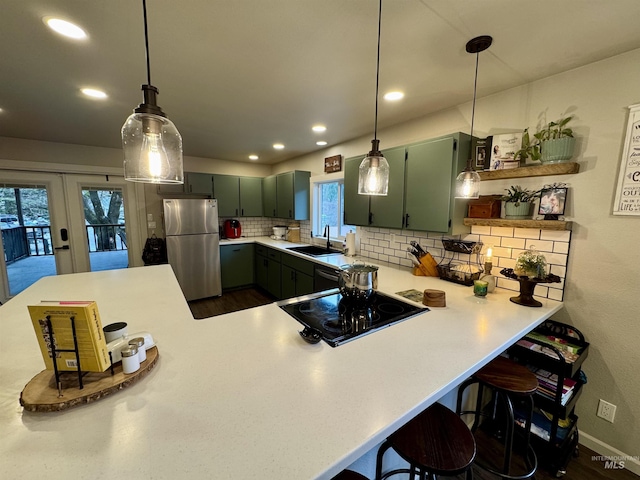 kitchen featuring cooktop, tasteful backsplash, freestanding refrigerator, a kitchen bar, and a sink