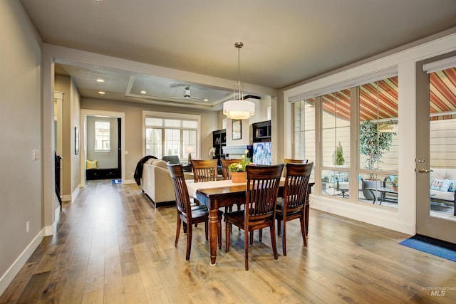 dining space featuring recessed lighting, wood-type flooring, a raised ceiling, and baseboards