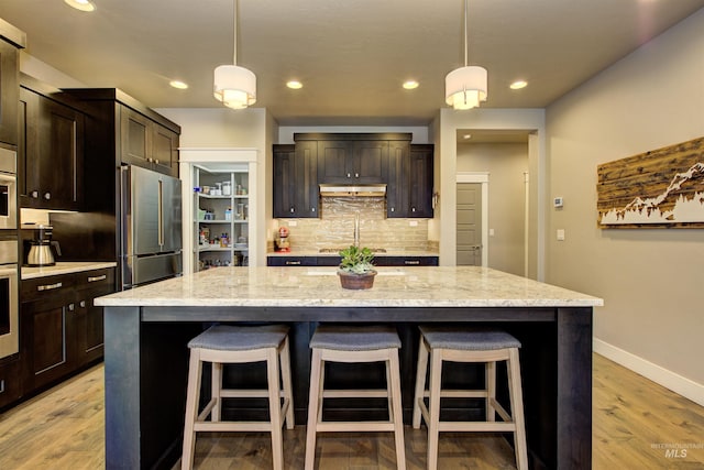 kitchen featuring appliances with stainless steel finishes, backsplash, light stone counters, and a kitchen breakfast bar