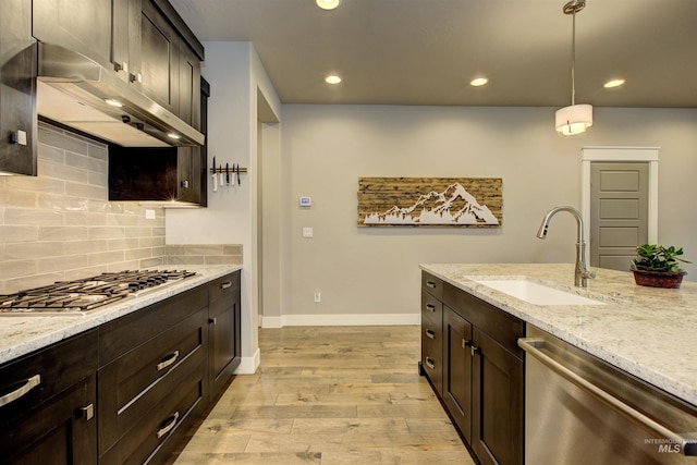 kitchen featuring light wood finished floors, stainless steel appliances, tasteful backsplash, a sink, and under cabinet range hood