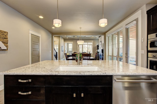 kitchen with an island with sink, light stone countertops, stainless steel appliances, pendant lighting, and recessed lighting