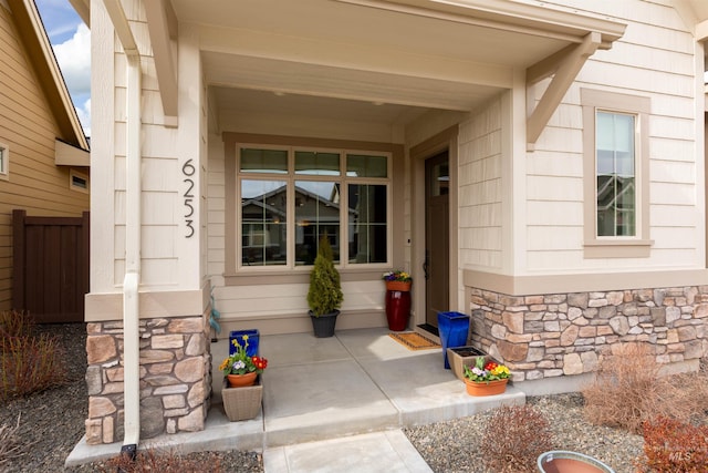 view of exterior entry featuring stone siding and fence