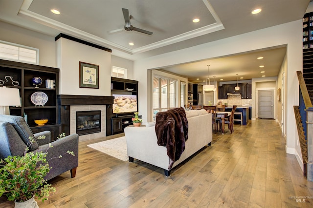 living room with a tile fireplace, light wood-type flooring, a raised ceiling, and recessed lighting