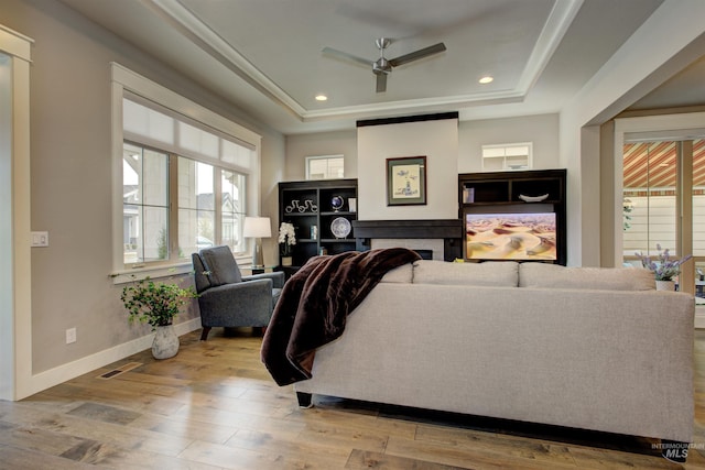 living room featuring a raised ceiling, visible vents, a fireplace, and wood finished floors