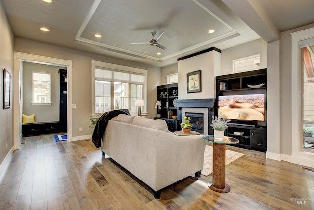 living area with recessed lighting, baseboards, light wood-style floors, a raised ceiling, and a glass covered fireplace