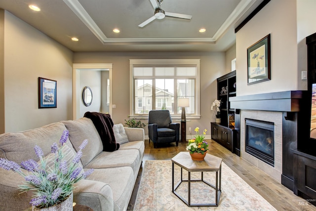 living area with light wood-style floors, recessed lighting, a raised ceiling, and a fireplace